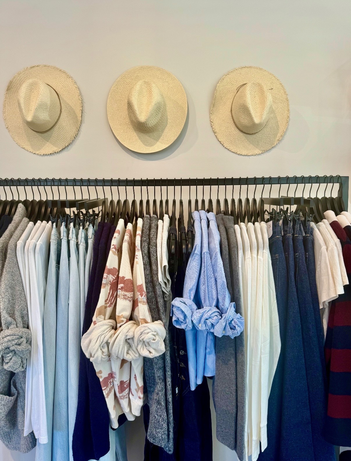 Blue, white, gray, and neutral apparel organized beneath three straw hats in Nantucket